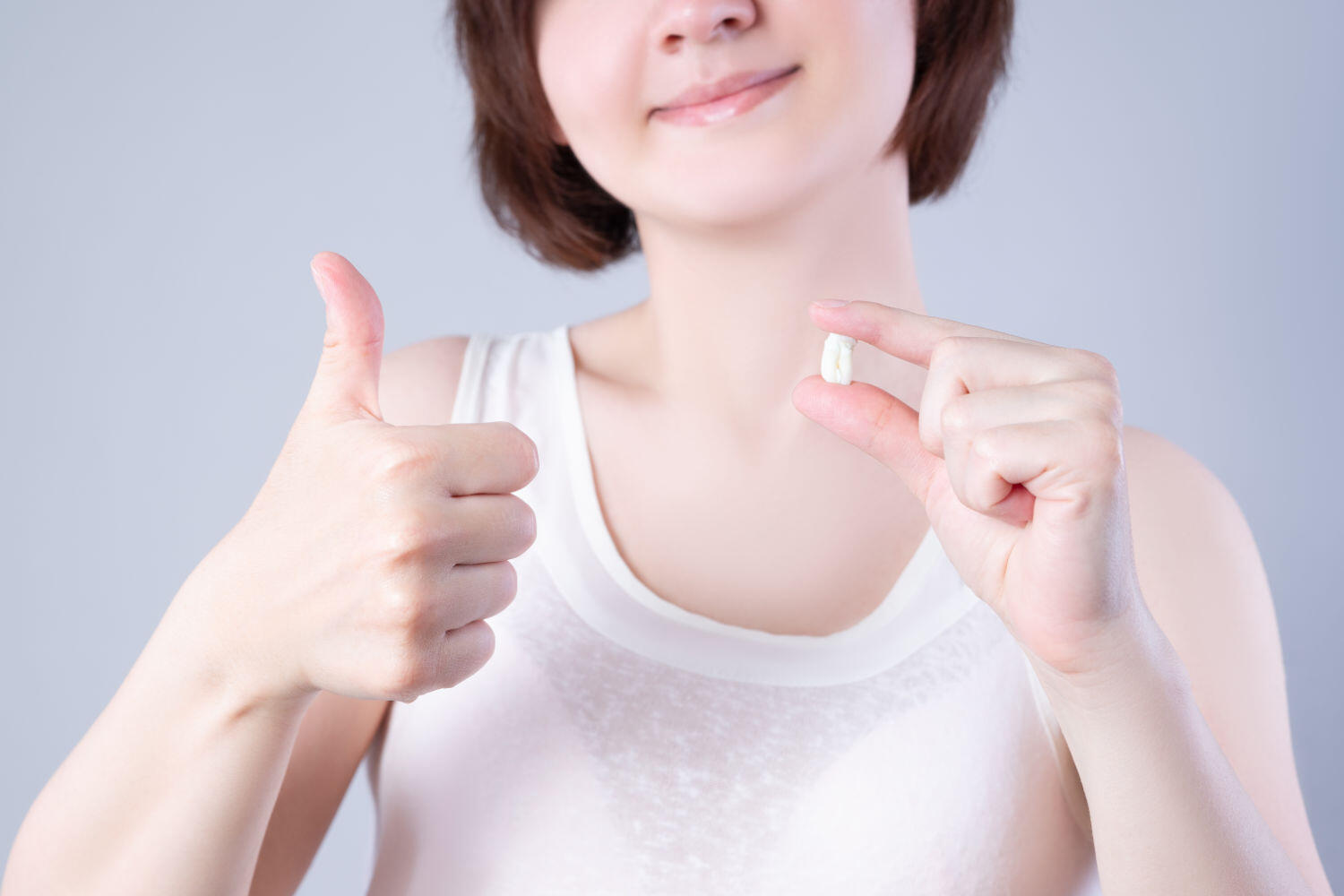 Wisdom teeth extraction, happy woman with tooth in hand on gray background